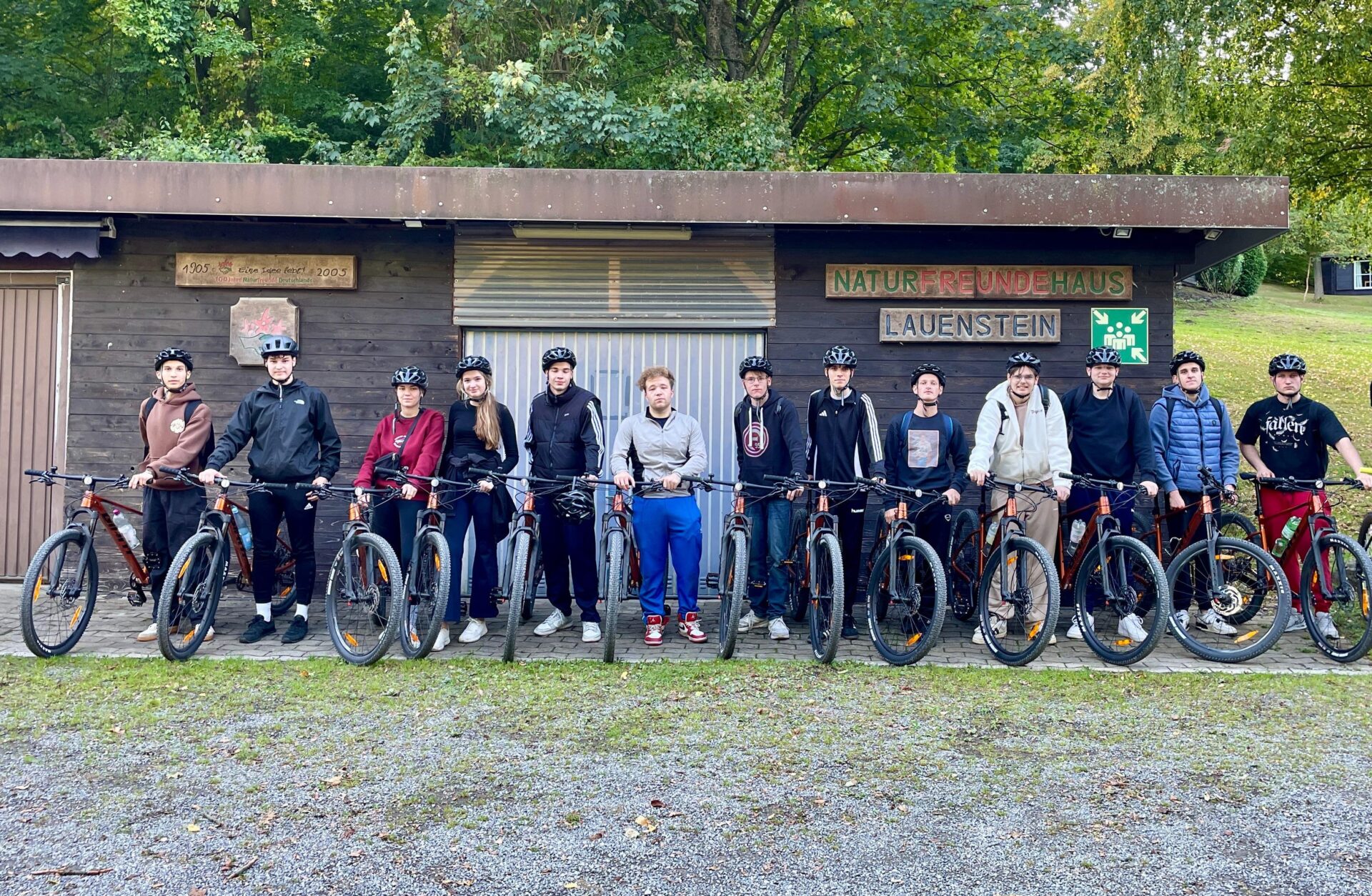 Schüler:innen der BBS Springe stehen mit Mountainbikes vor einem Holzhaus auf dem der Schriftzug "Naturfreundehaus Lauenstein" zu lesen ist.