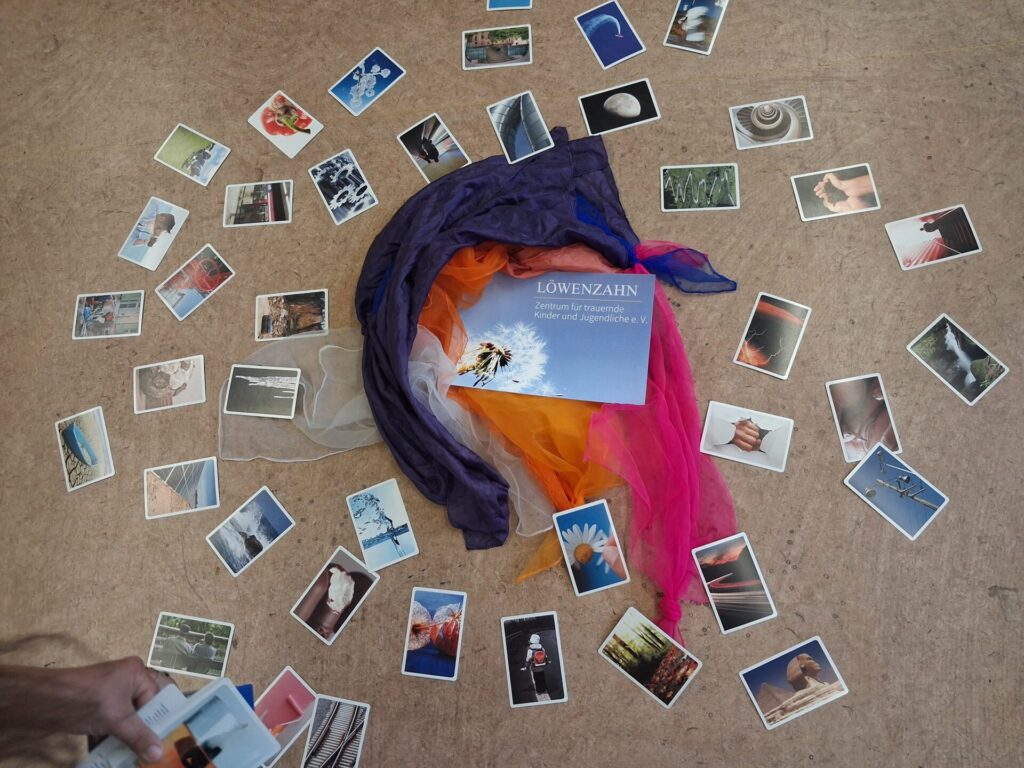Verschiedene Fotos und Tücher zum Thema Kindertrauer sind auf einem Fußboden ausgebreitet.