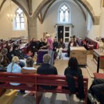 Schüler:innen sitzen in einer Kirche auf Kirchenbänken und bekommen die Funktion von Orgelpfeifen erklärt